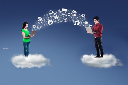Two business people standing on cloud and use laptop computer to send informationの写真素材