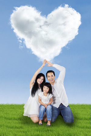Young asian family sitting on meadow under cloud shaped heartの写真素材