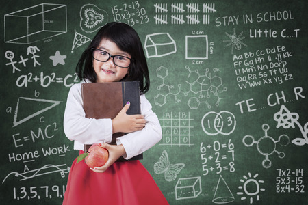Learning concept with cute little girl holding a book and apple in classsroomの写真素材