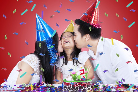 Two asian parents kiss their daughter in birthday partyの写真素材