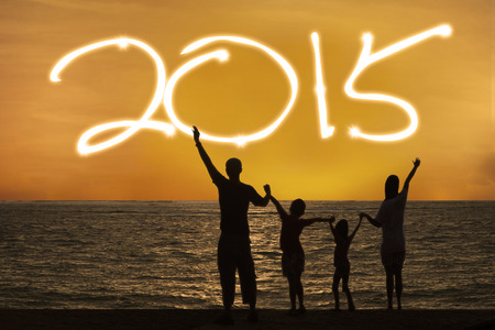 Silhouette of happy family on beach with number 2015 on the sky