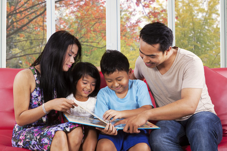 Cheerful asian children read a story book with their parents at home in autumn dayの写真素材