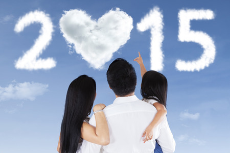 Rear view of happy family looking and pointing at cloud shaped a number 2015