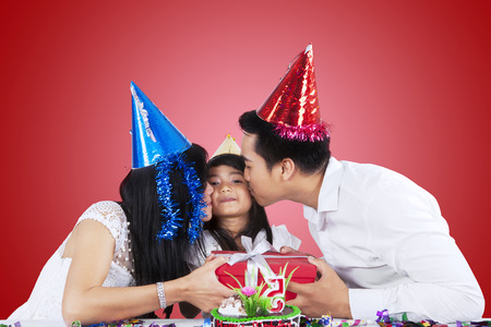 Portrait of little girl receiving a gift and kiss from her parents in birthday partyの写真素材