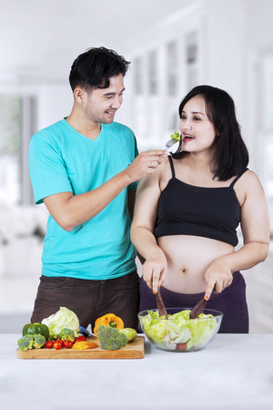 Portrait of asian husband giving healthy food to his pregnant wife in the ktichenの写真素材