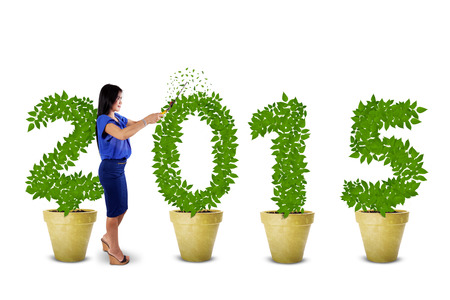 Businesswoman using a scissors to nurture the trees shaped number 2015, symbolizing a manager in investmentの写真素材