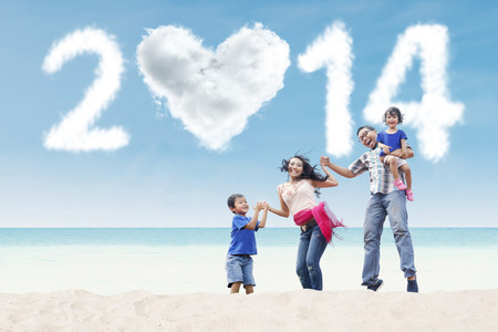 Happy family having fun in the beach with heart shaped cloud of new year 2014の写真素材