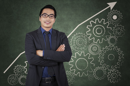 Portrait of confident businessman smiling at camera in front of chart and cogwheelの写真素材