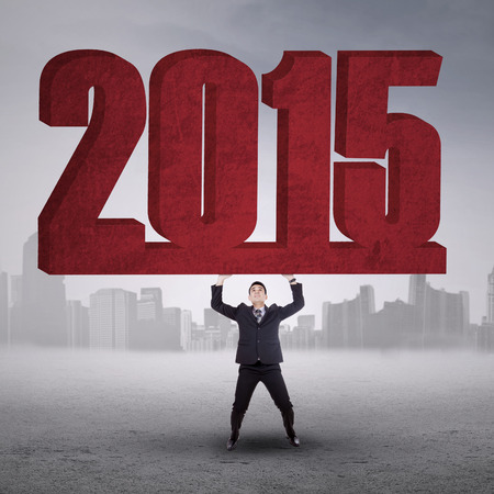 Portrait of businessman lifting number 2015 to celebrate new year outdoors