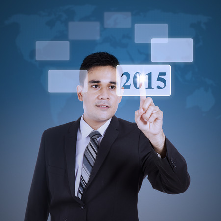 Young male worker pressing number 2015 on virtual screen with blue backgroundの写真素材