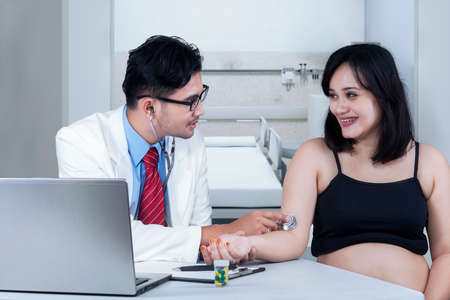 Expectant woman sitting in consulting room while doctor checking blood pressureの写真素材