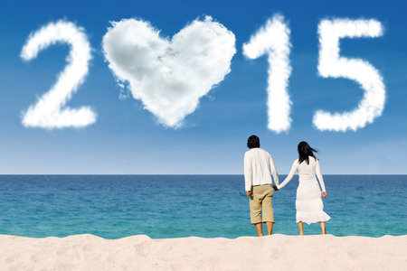 Young couple holding hands on beach and looking at cloud shaped number 2015