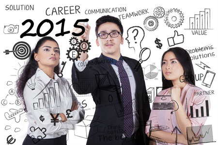 Three multiracial businesspeople making strategy for 2015 on whiteboardの写真素材