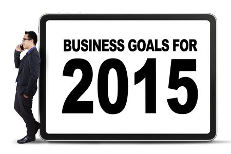 Young businessman talking on the phone while leans on a board of business goals for 2015