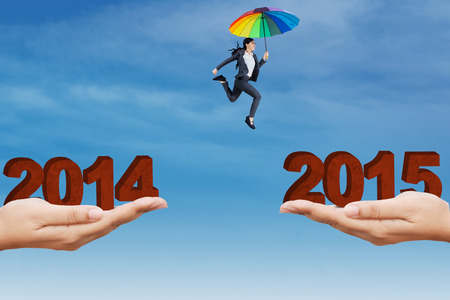 Young businesswoman using colorful umbrella to leap through a gap with numbers 2014 to 2015