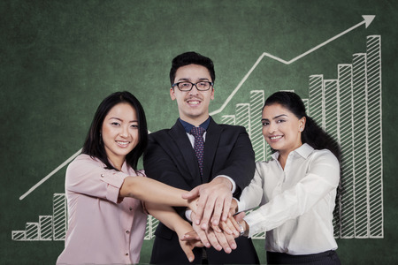 Portrait of businesspeople joining hands while smiling at the camera in front of business chartの写真素材