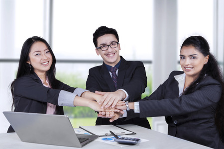 Portrait of three business people smiling at the camera while joining hands