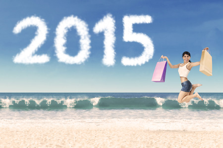 Cheerful woman holding shopping bag jumping at beach celebrate new year of 2015の写真素材