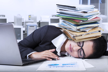Female entrepreneur with tired expression sleeping in the office with paperwork on her head
