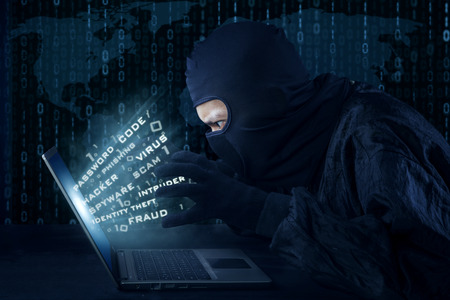 Side view of unknown hacker with mask stealing information from laptop computer