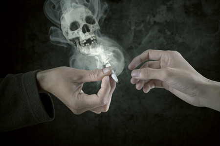 Closeup of hands sharing cigarette with smoke shaped skullの写真素材