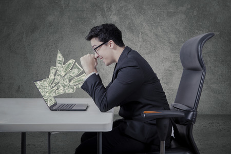 Cheerful caucasian businessman looking money dollars from laptop comoputerの写真素材