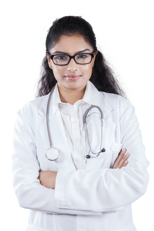 Young asian doctor smiling at the camera while wearing uniform and folding hands in studioの写真素材