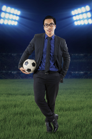 Full length of a young businessman standing at field while holding a soccer ballの写真素材