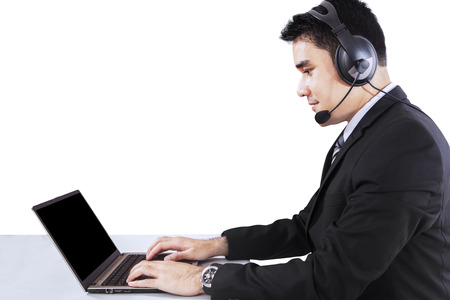 Young businessman working on laptop and using a headphone, isolated on white background