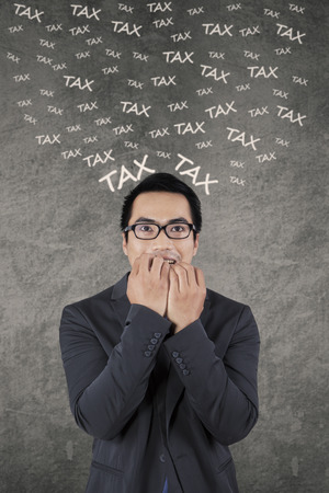 Stressful businessman biting his nail while thinking his tax, shot against gray backgroundの写真素材