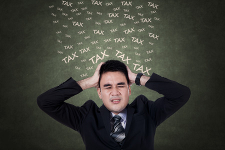 Expressive businessman in business suit thinks tax while holding his headの写真素材