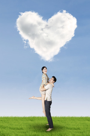 Full length of couple enjoy holiday and having fun under heart shaped cloud on the meadowの写真素材