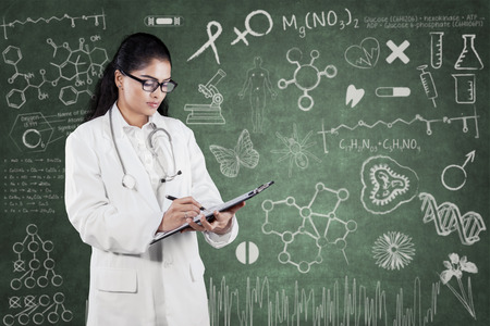 Portrait of young female doctor writes on clipboard with doodle on the chalkboard