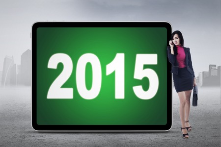 Beautiful businessperson standing outdoors while talking on the phone and lean on board with numbers 2015の写真素材