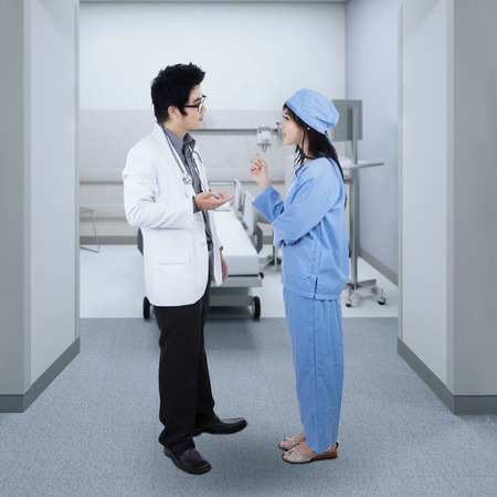 Full length of male doctor standing in the hospital while talking with a female surgeonの写真素材