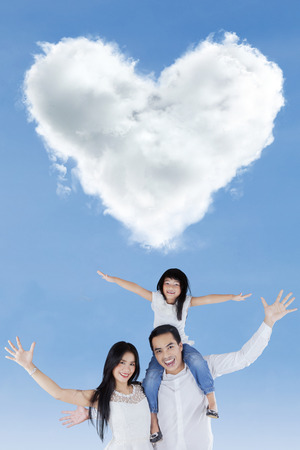 Portrait of cheerful family raise hands together and enjoy freedom under cloud shaped heartの写真素材