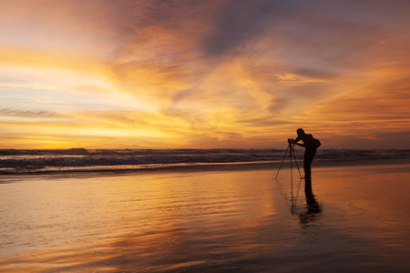 Male photographer taking picture with dslr camera on the beach at sunset timeの写真素材