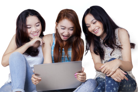 Group of three cheerful teenage girls sitting on the floor in the studio while using laptop computerの写真素材