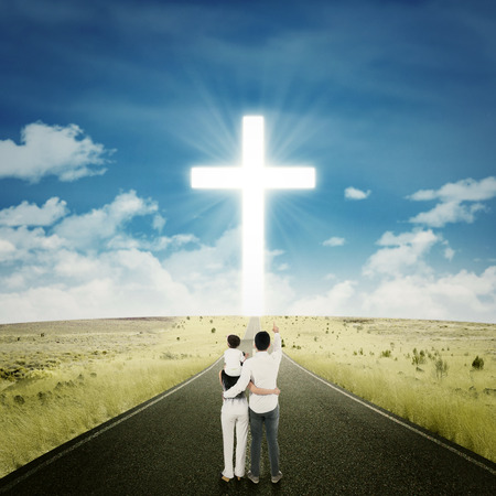 Young family standing on the highway and looking at a cross on the end of the roadの写真素材
