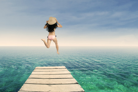 Happy woman wearing bikini jumping on the pier at beachの写真素材