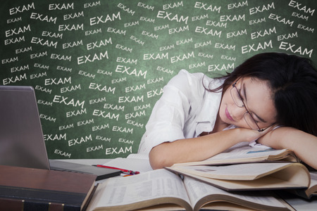 Beautiful teenage student sleeping above textbooks on desk after studying for examの写真素材