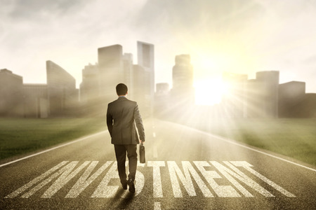 Successful businessman carrying a briefcase and walk on the road with an investment text Successful businessman carrying a briefcase and walk on the road with an investment text