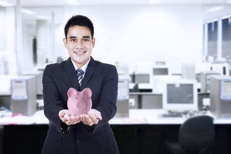Portrait of young businessman smiling and holding a piggy bankの写真素材