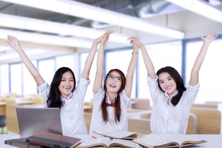 Three successful female students raise hands together in the classroomの写真素材