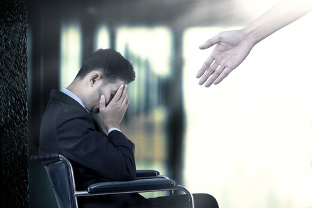 Frustrated businessman sitting on a wheelchair,  get a help from a hand