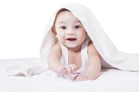 Portrait of cheerful male toddler crawling on bed under a towel, isolated on white backgroundの写真素材