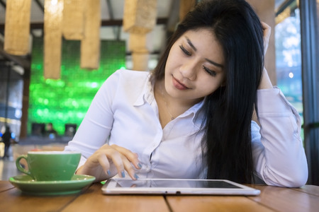 Portrait of attractive female worker using tablet while sitting in the cafe and enjoying hot coffee