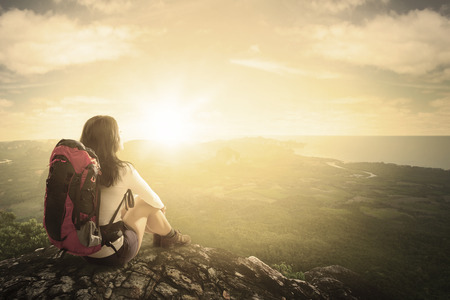 Rear view of female hiker with backpack, sitting on the rock while enjoying a valley viewの写真素材