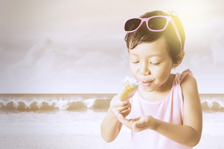 Beautiful little child holding and enjoying a melted ice cream on the beachの写真素材