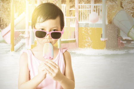 Portrait of happy little girl standing at the pool while wearing sunglasses and enjoy ice creamの写真素材